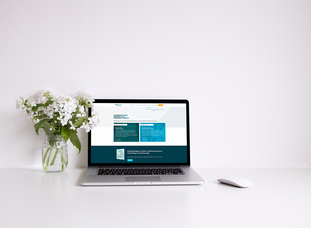 Laptop on a white desk displaying a website focused on strategic partnerships, accompanied by a vase of white flowers. The setup highlights a clean and modern workspace ideal for productivity and creativity.